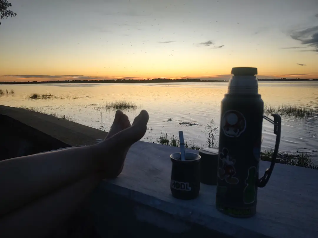 Un termo y los pies apoyados en el borde, frente a la laguna.