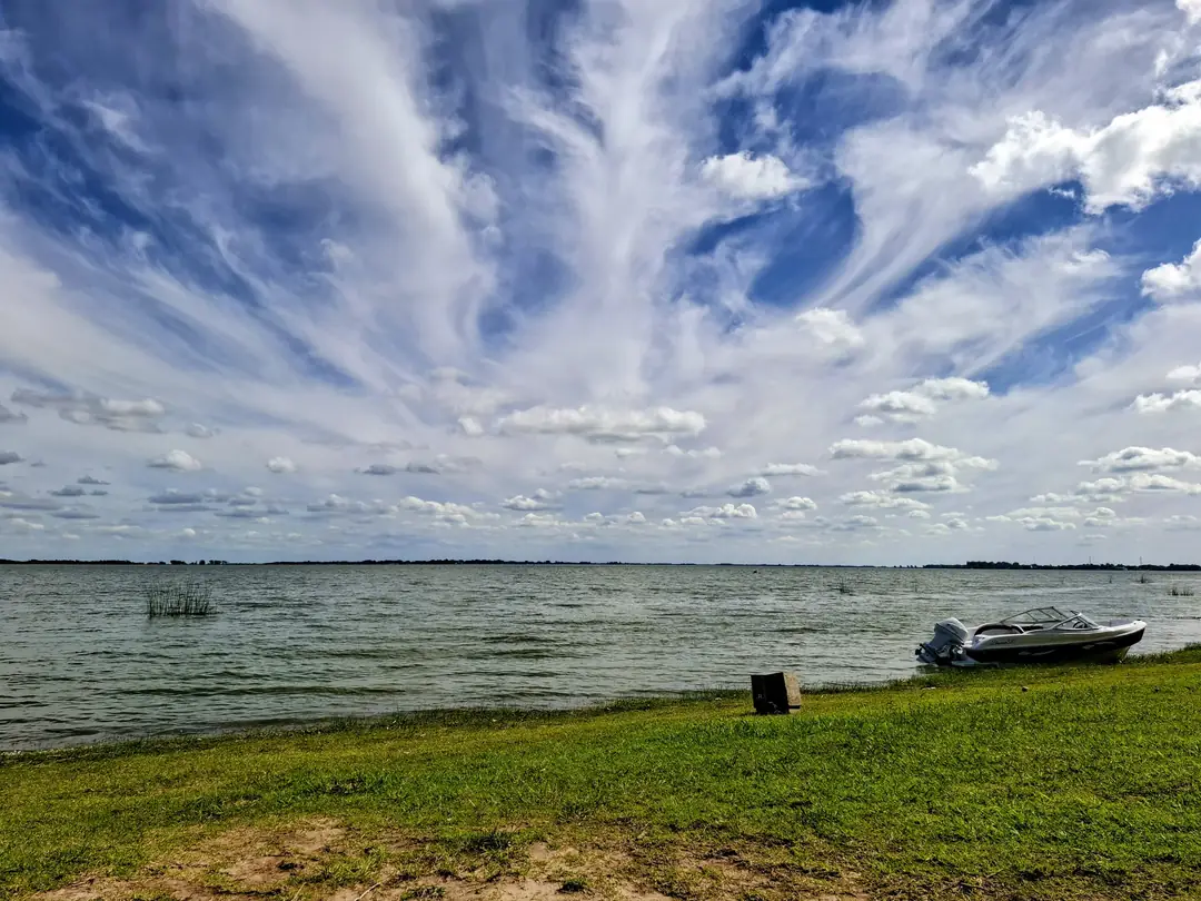 La laguna de Chascomús desde la orilla del complejo, con una lancha y el cielo con nubes.