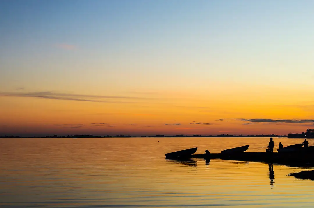 Botes en la orilla de la laguna de Chascomús, con el cielo naranja.
