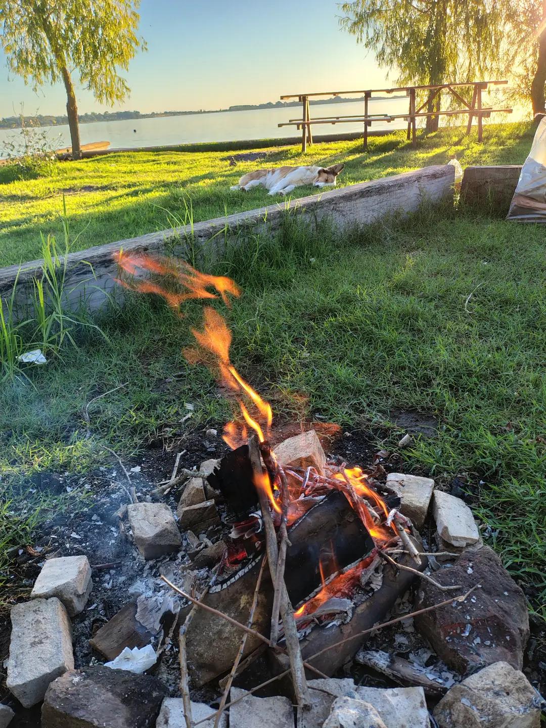 El fuego de un fogón sobre el pasto, con la laguna atrás.
