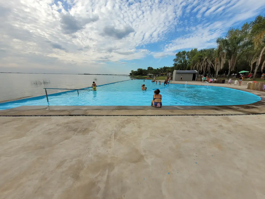 La pileta infinita con gente en el agua y el cielo con nubes.