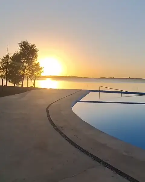 La pileta infinita con el sol bajo sobre la laguna.