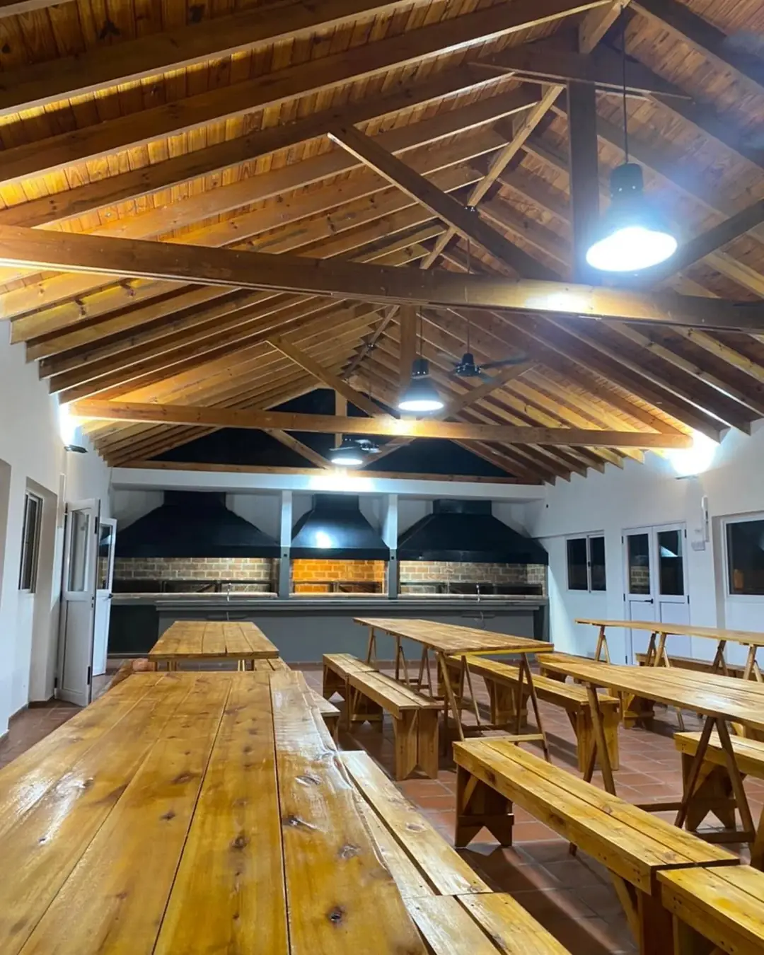 El SUM con techo de madera, mesas largas y las parrillas al fondo.